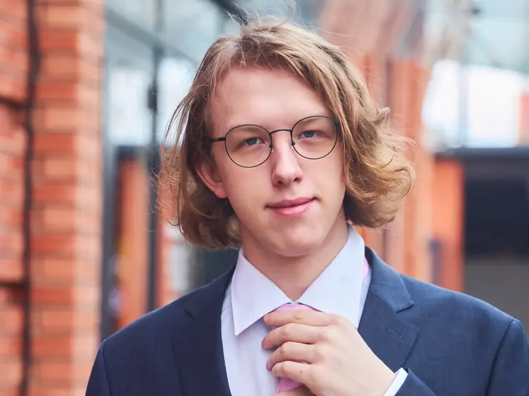 A student in a suit, adjusting his tie