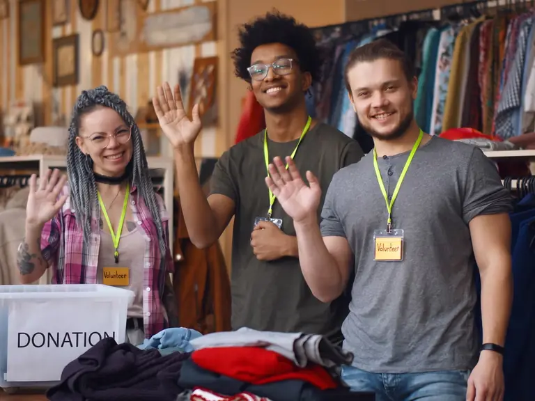 Three volunteers waving behind a donations table