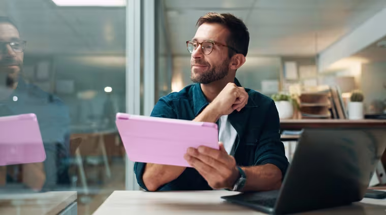 A programme participant looking up from a tablet at his desk in a glass-walled office.