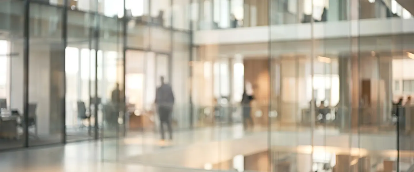 An open, glass-walled university building, seen through several layers of glazing.