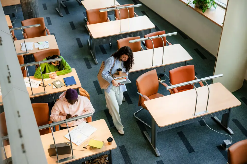 Students working at desks in a university library, seen from above.