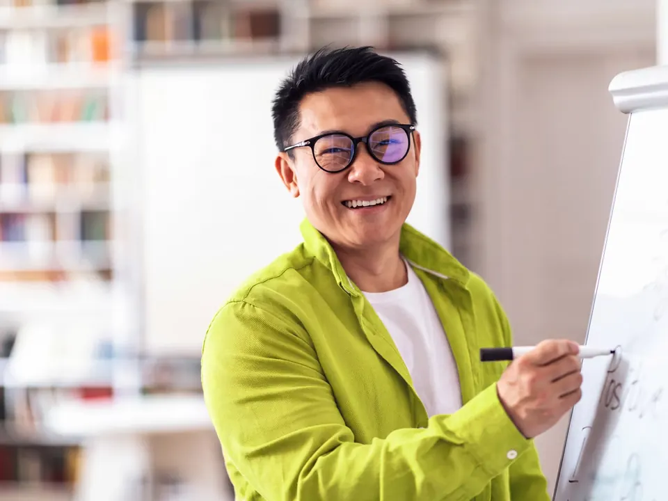 An academic smiling as he writes on a whiteboard.